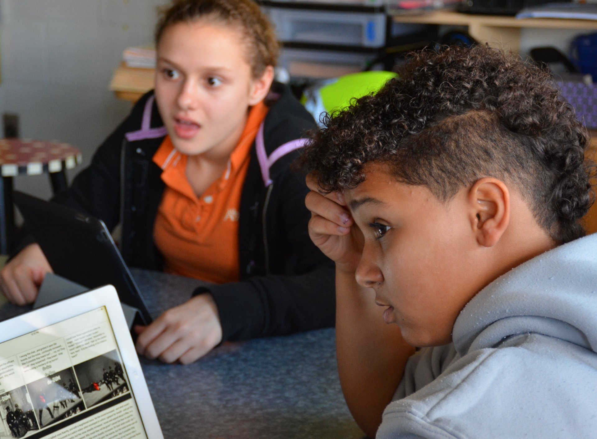 Two students looking intently at a laptop screen displaying the Amplify ELA curriculum in a classroom setting, one resting their head on their hand.