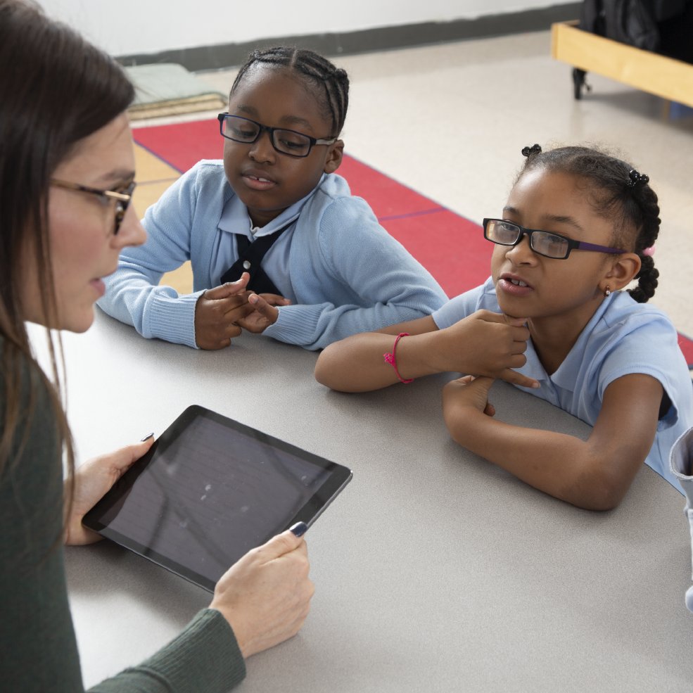A teacher using a tablet with two students at a table
