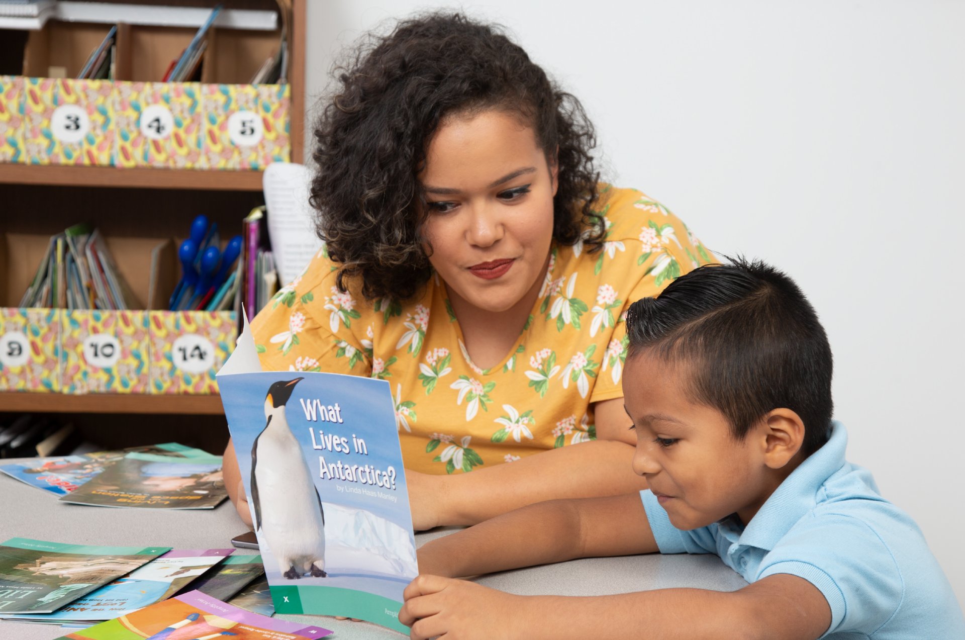 A teacher helping a student read the book What Lives in Antartica?