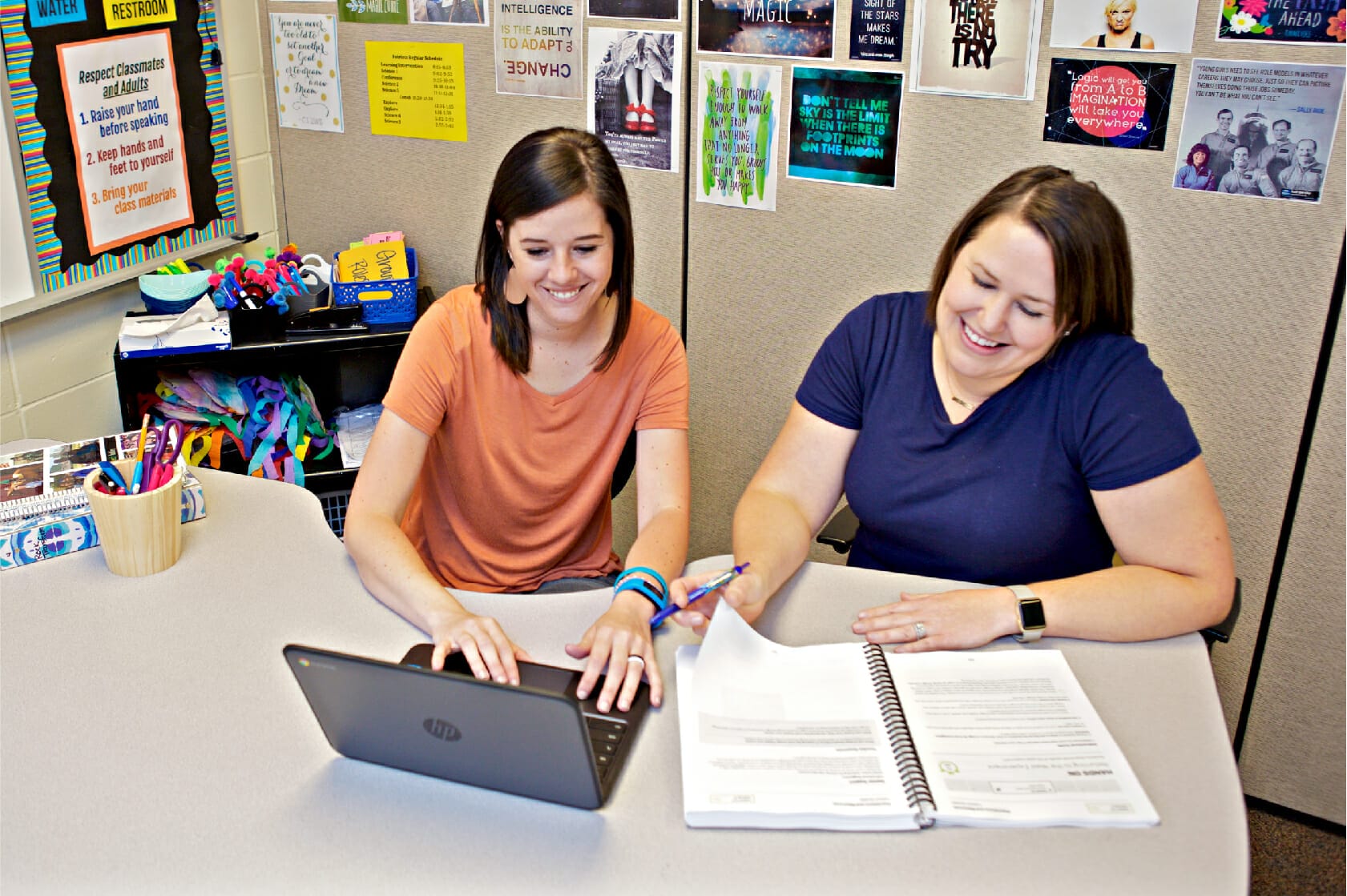 Two teachers working together and using a laptop and notebook