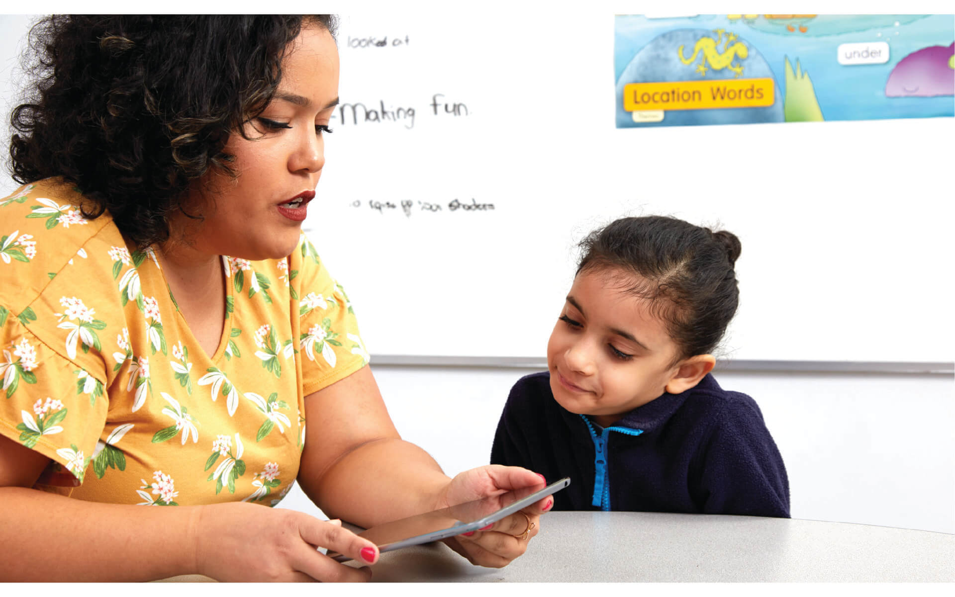 A teacher using a tablet and working with a student