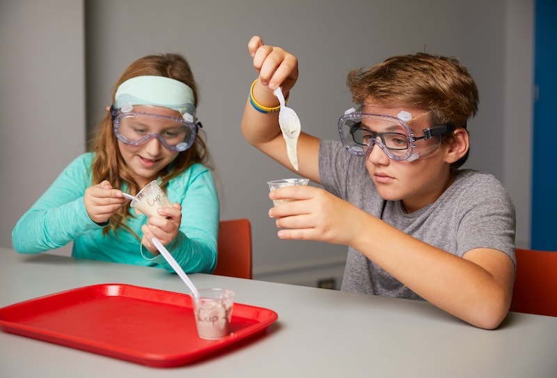 Two children in safety goggles conducting a science experiment with liquids in a classroom.