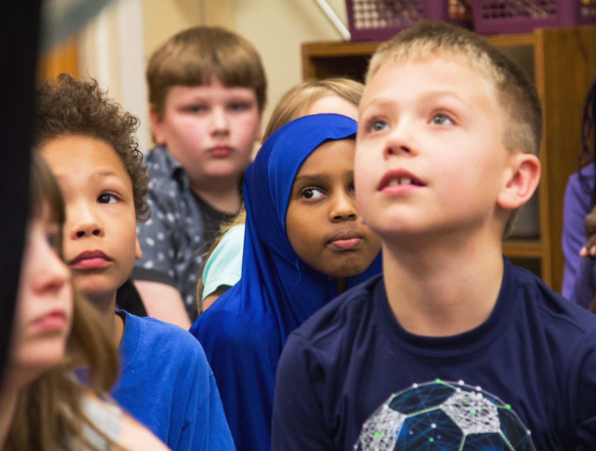 A group of diverse children attentively looking upwards with expressions of curiosity and interest.
