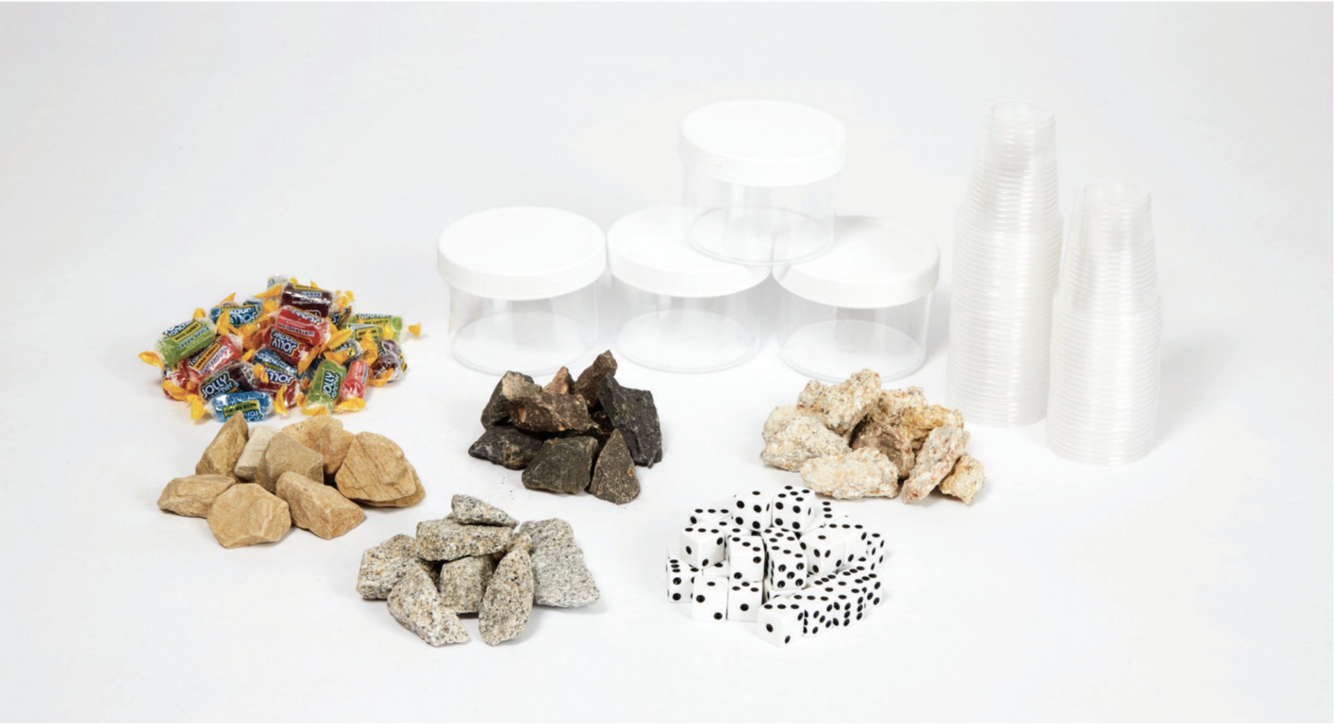 Several groups of materials, including candies, various rocks, clear plastic containers, and stacked plastic cups, arranged on a white surface.