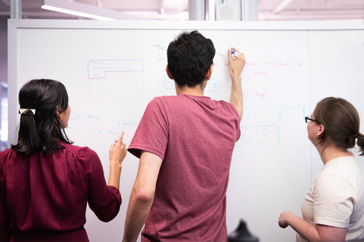 Three people draw on a whiteboard in an office