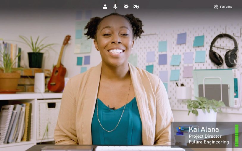A smiling black woman with her hair in a bun, wearing a teal top and beige cardigan, sits at a desk in an office with musical instruments and coding textbooks in the background.