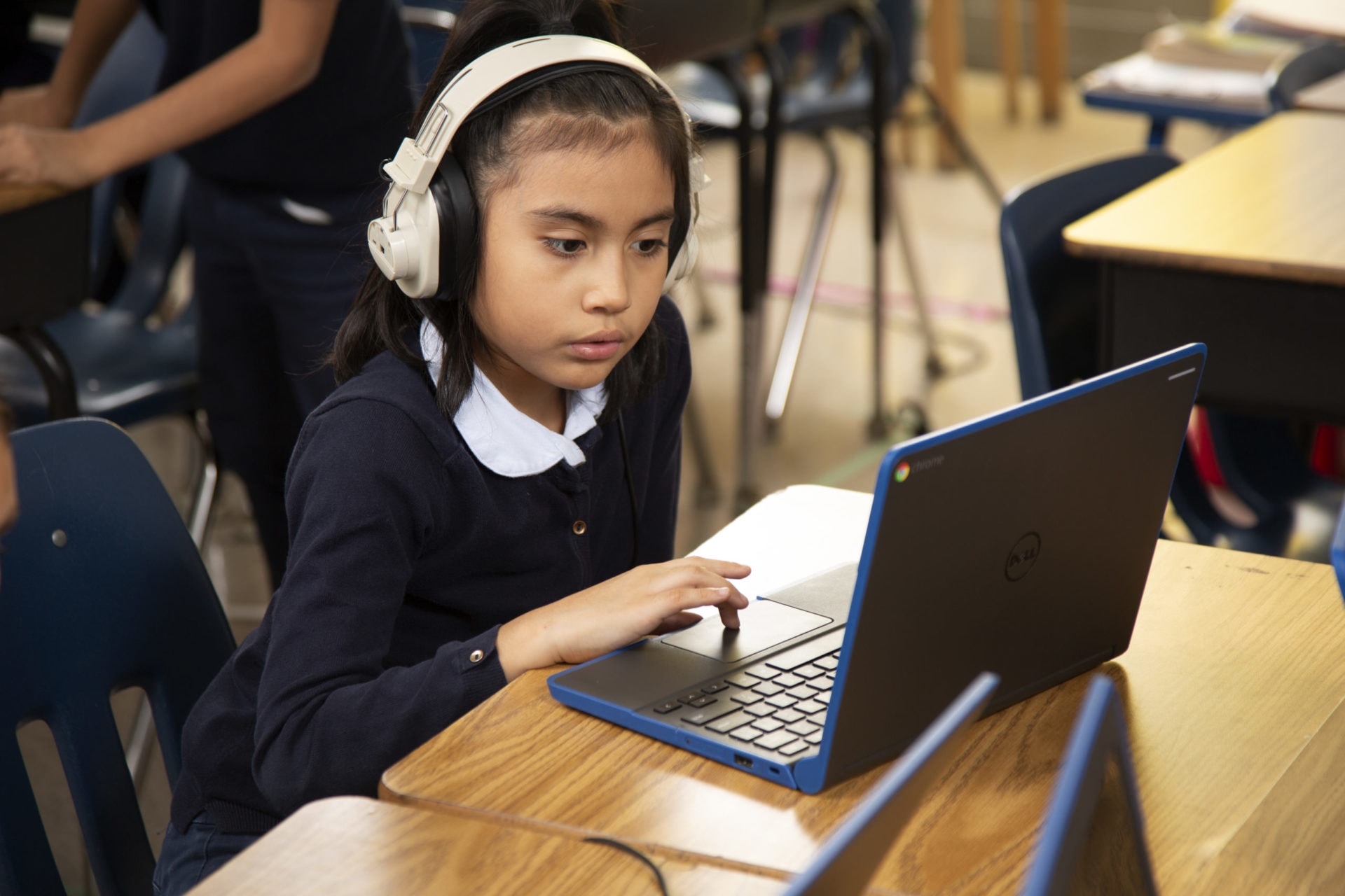 Young student in headphones using a laptop at an LAUSD classroom desk.
