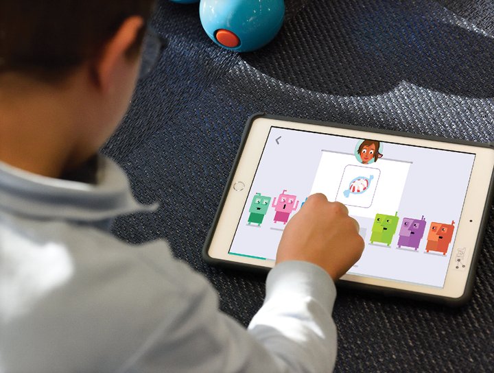 A child interacts with a K-5 personalized learning program on a tablet, pointing to a colorful graphic of bears displayed on the screen.
