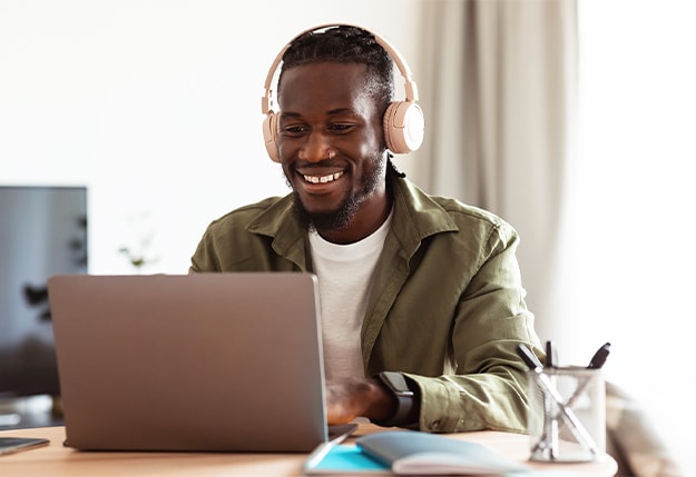 Man with headphones smiling while listening to a science of reading podcast and using a laptop at a desk.