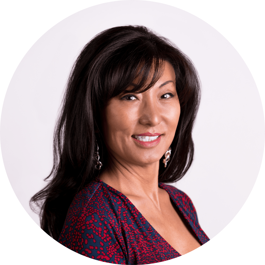 A professional headshot of a middle-aged asian woman with shoulder-length black hair, wearing a red and black patterned top and earrings, smiling against a white background.