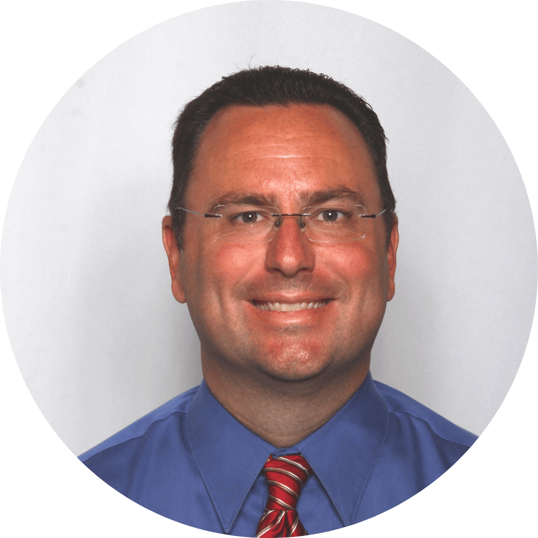 A smiling caucasian man wearing glasses, a blue shirt, and a red striped tie in a professional headshot.