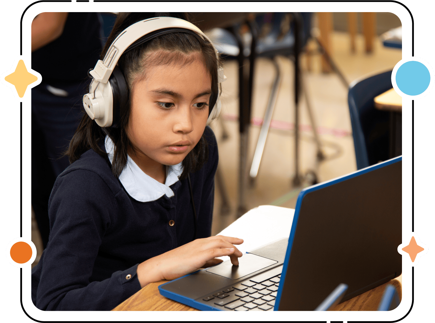 Una niña que usa audífonos y usa una computadora portátil en un salón de clases, concentrada en su pantalla con una computadora portátil a su lado, participa en programas de alfabetización bilingüe.