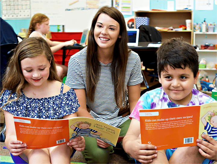 A teacher and two students sitting on the floor, reading books together in a colorful classroom as part of a K-8 literacy program.