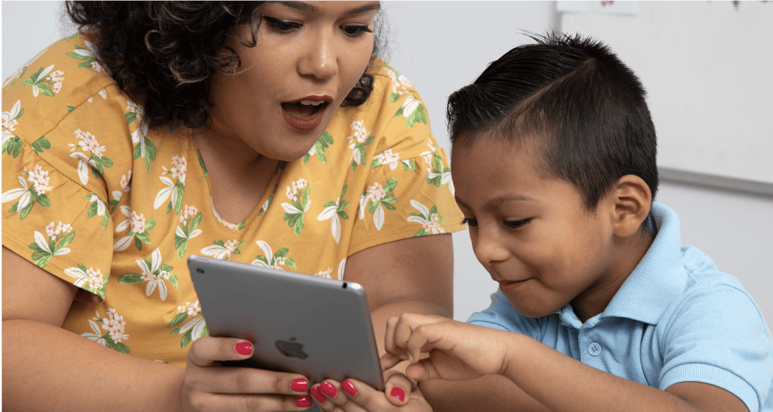 A woman and a young boy look at a tablet together with expressions of surprise and engagement.