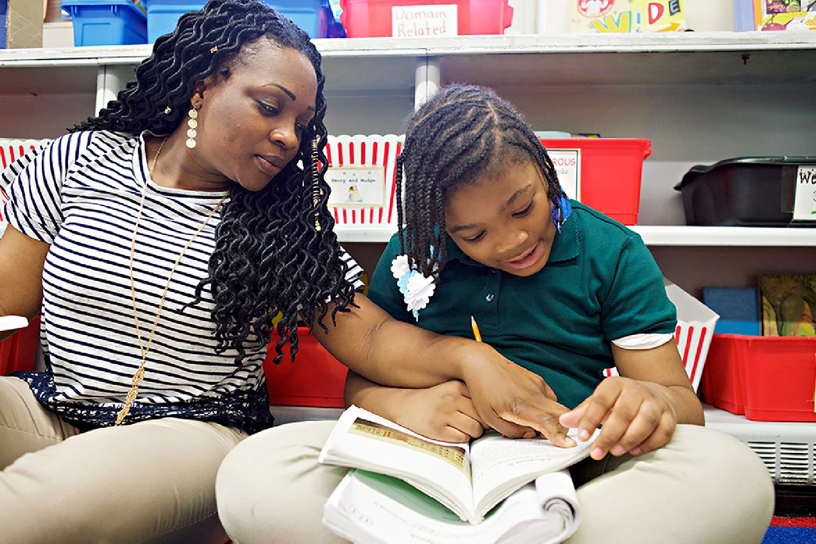 A woman and a young girl reading a book together in a classroom setting, surrounded by science of reading resources.