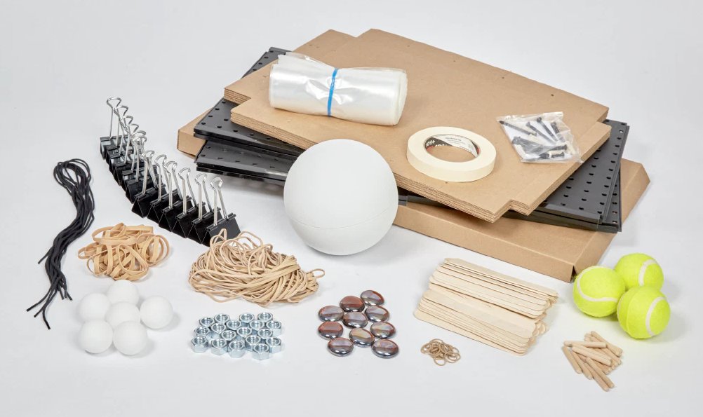 Assorted office and household items displayed on a white background, including rubber bands, binder clips, cardboard, and sports balls.