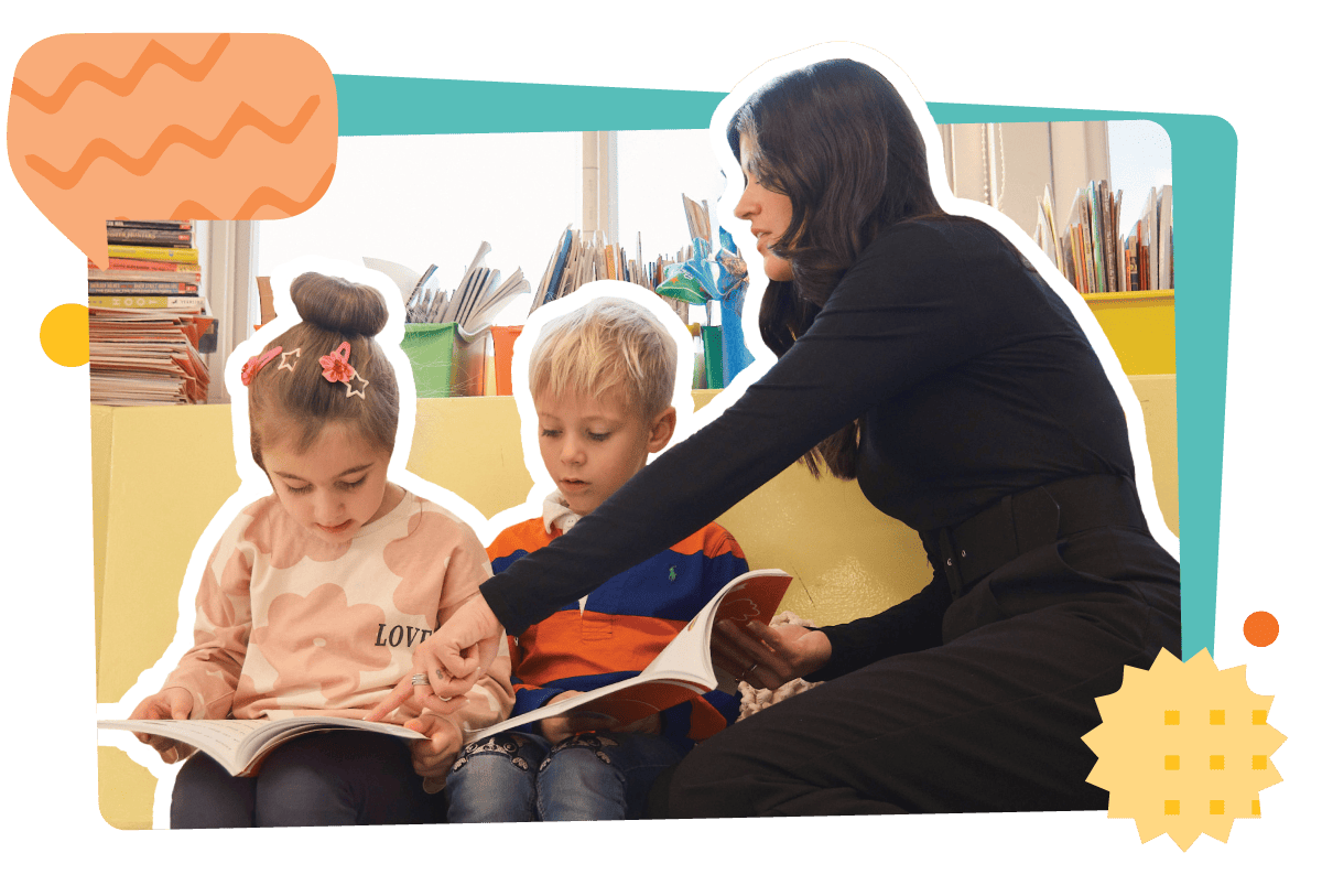 A woman sits reading a book to two young children on a couch in a colorful library setting.
