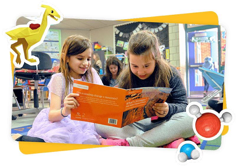 Dos niñas se sientan en el suelo de un aula leyendo un libro juntas, rodeadas de decoraciones coloridas.